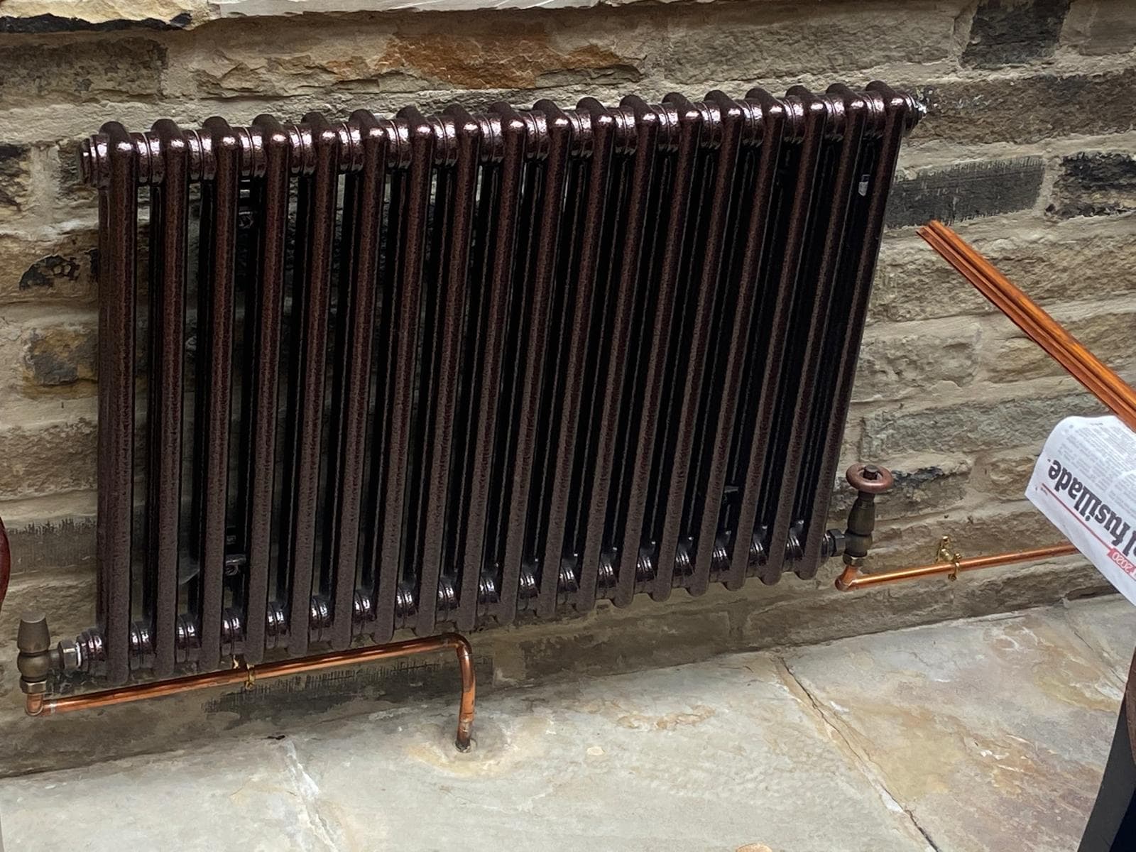 Cast iron column radiator on a stone wall with exposed copper pipework and period valve