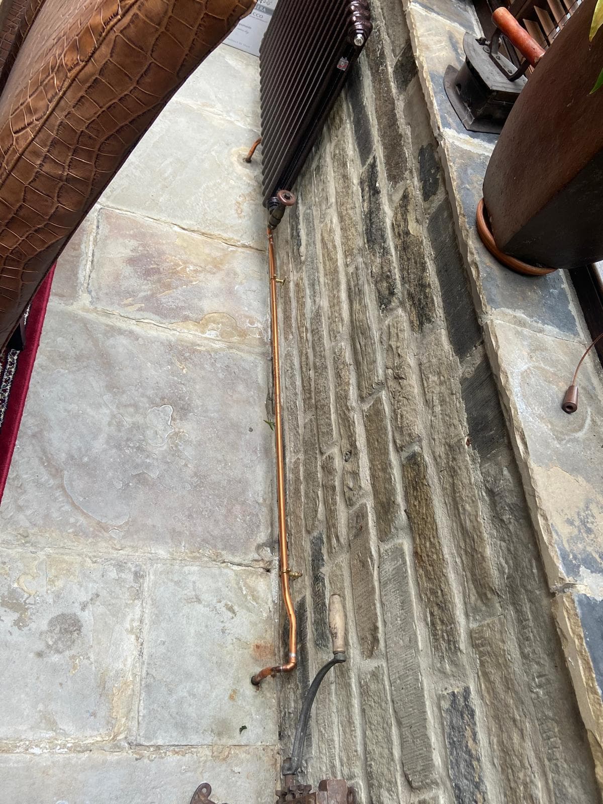 Exposed copper pipe run dressed along a stone wall to a cast iron radiator