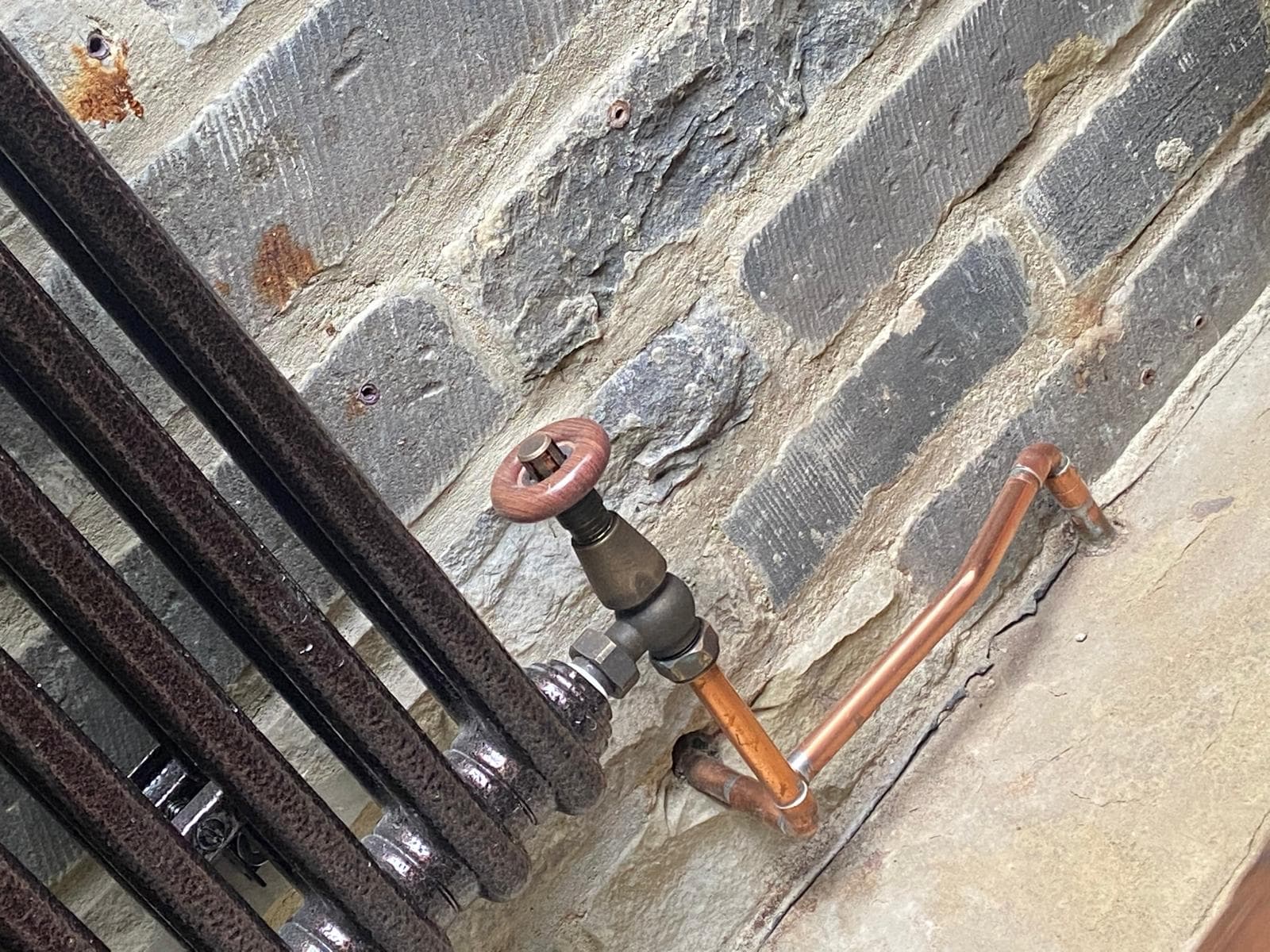Period-style radiator valve with wooden wheel head and copper bends on a brick wall