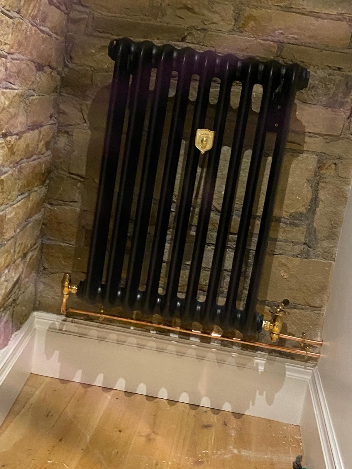 Black cast iron column radiator with brass valves against an exposed stone chimney breast