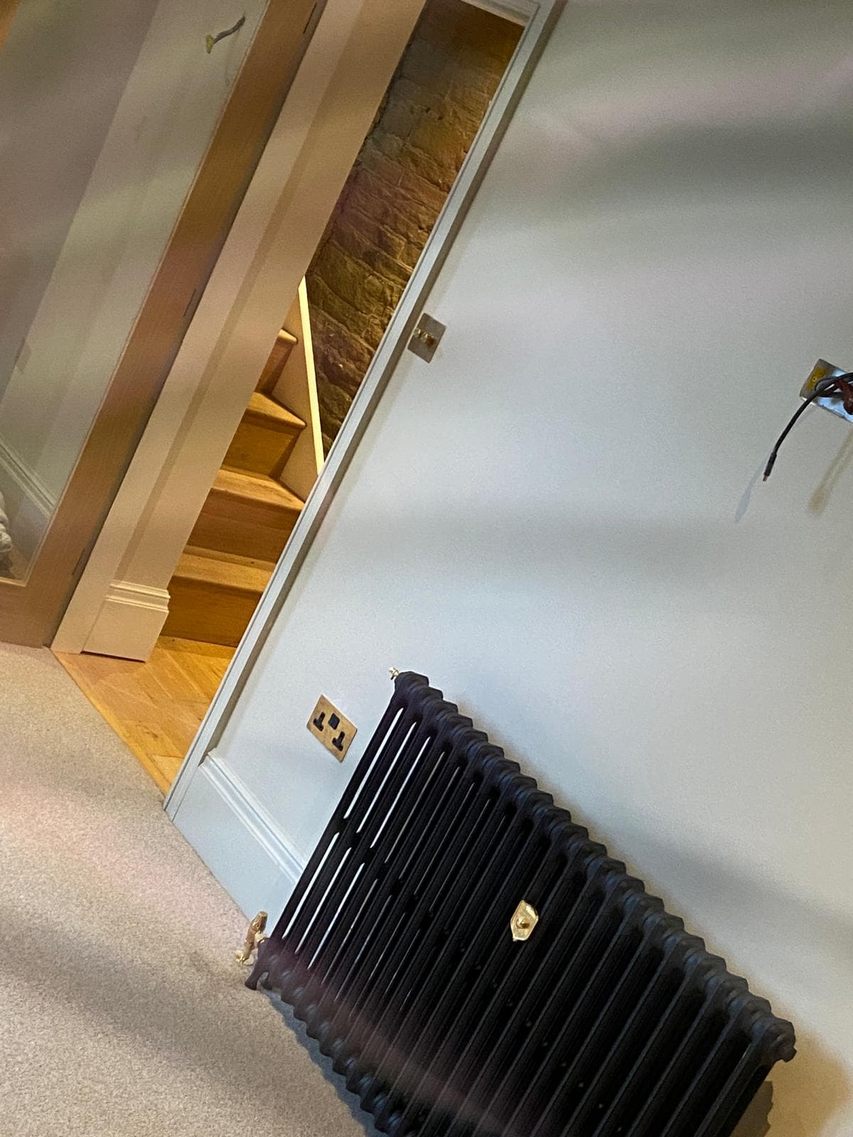 Black column radiator with brass valves in a period hallway