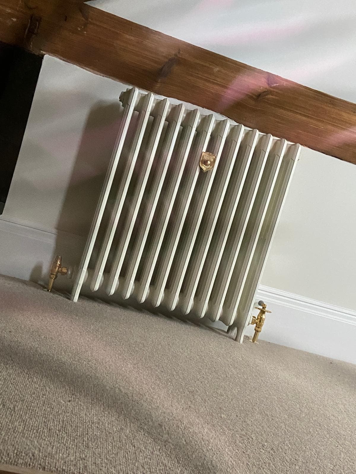 White column radiator with brass valves fitted in a beamed attic room