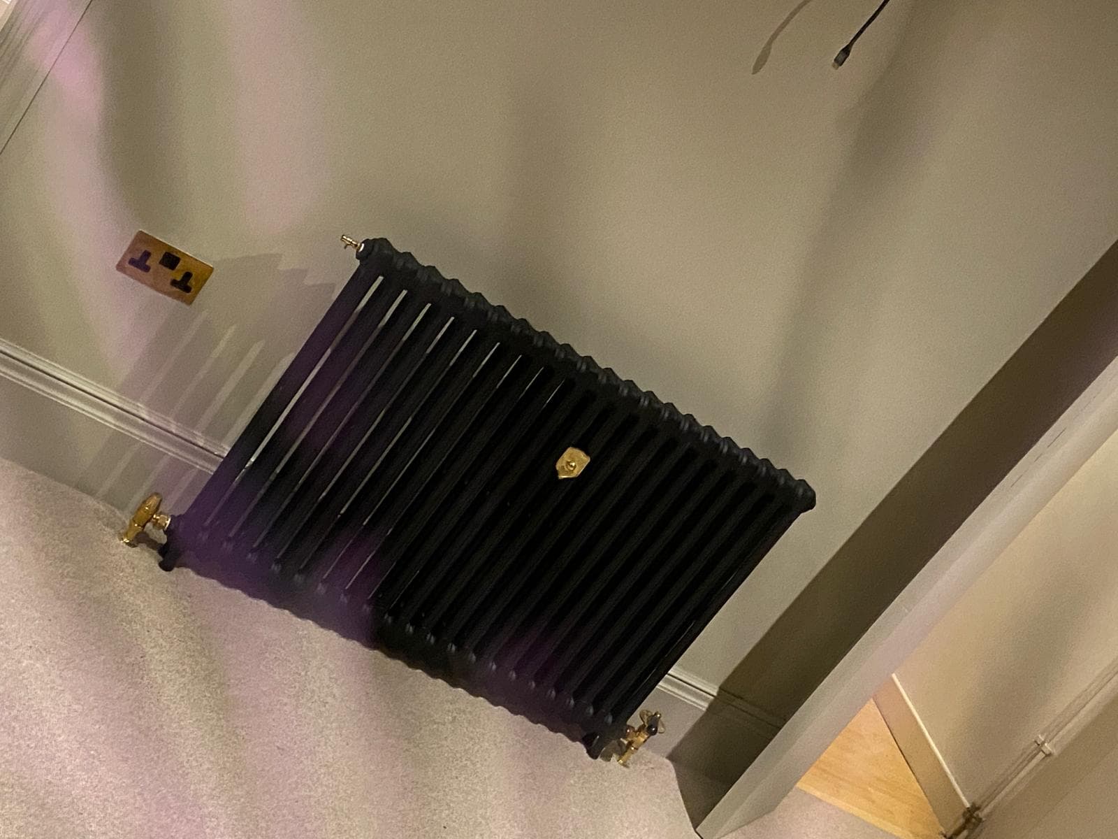 Dark column radiator with brass valves on a modern grey wall