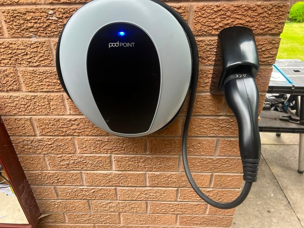 Pod Point Solo home EV charger with tethered cable and holster mounted on a brick wall
