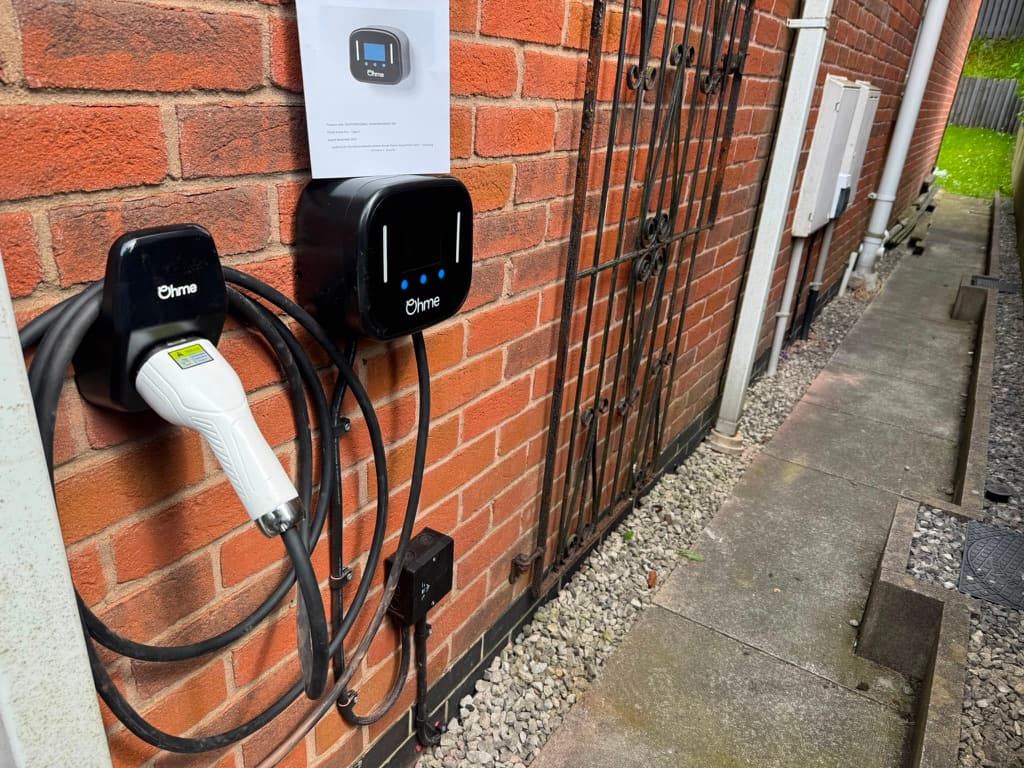 Ohme ePod EV charger installed on a brick wall with the charging cable holstered alongside