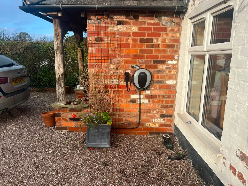 Compact oval EV charge point neatly installed on the brick wall of a country cottage driveway