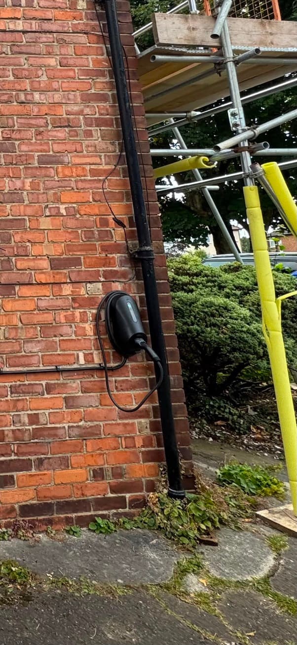 Tethered smart EV charger mounted on a brick corner wall beside the driveway