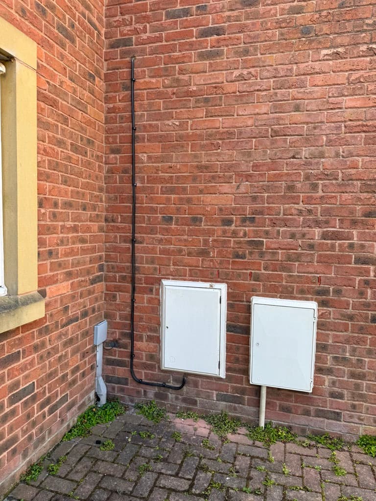 Neatly clipped EV charger supply cable run down the wall past the meter boxes