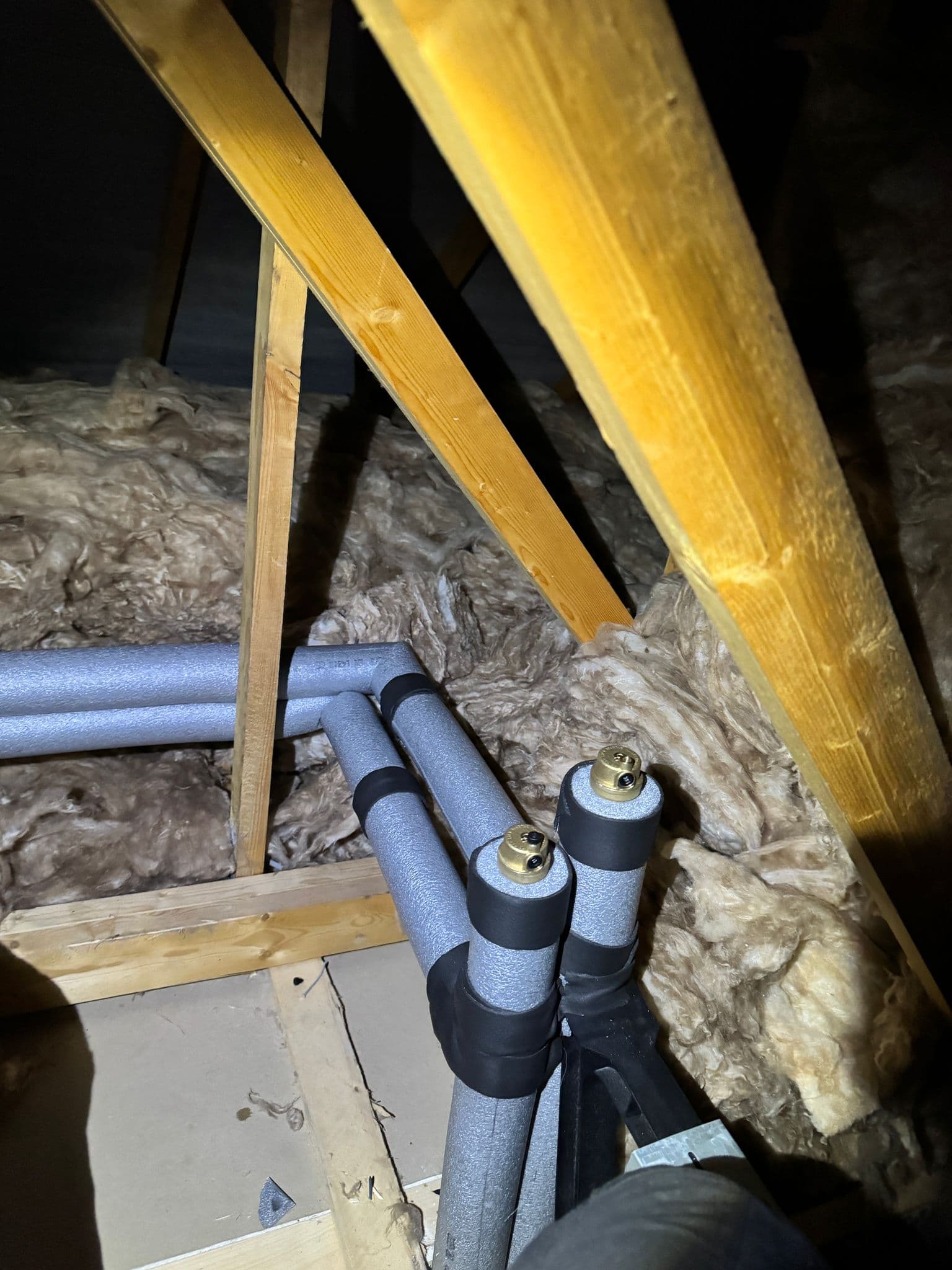 Heating pipework insulated with foam lagging in a loft, with automatic air vents fitted